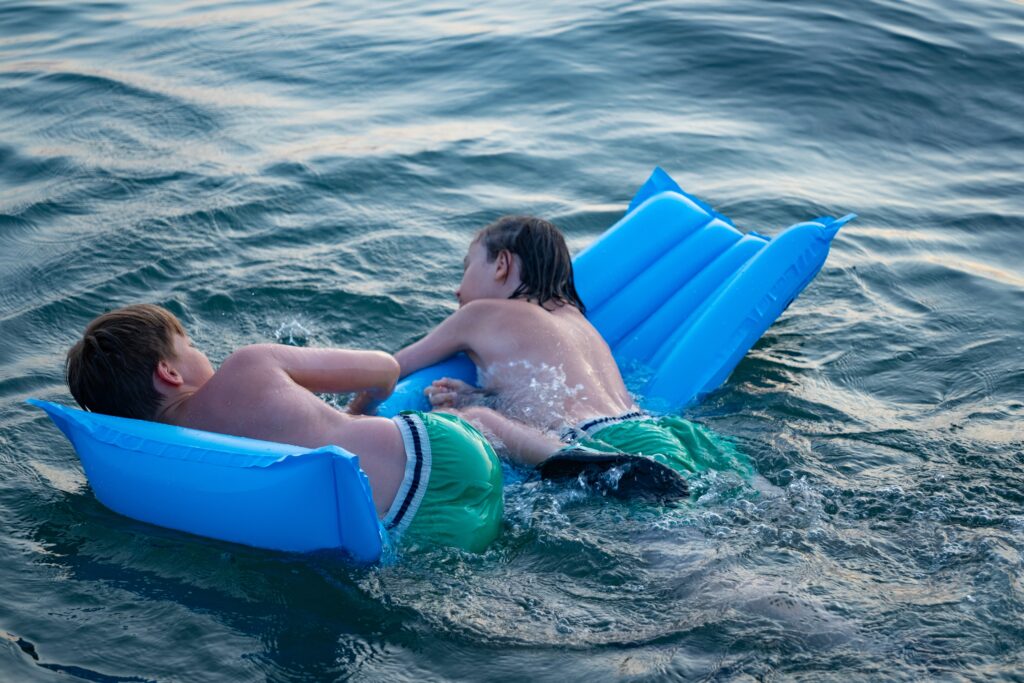 two,children,swimming,in,sea,,adrift,on,blue,inflatable,raft,