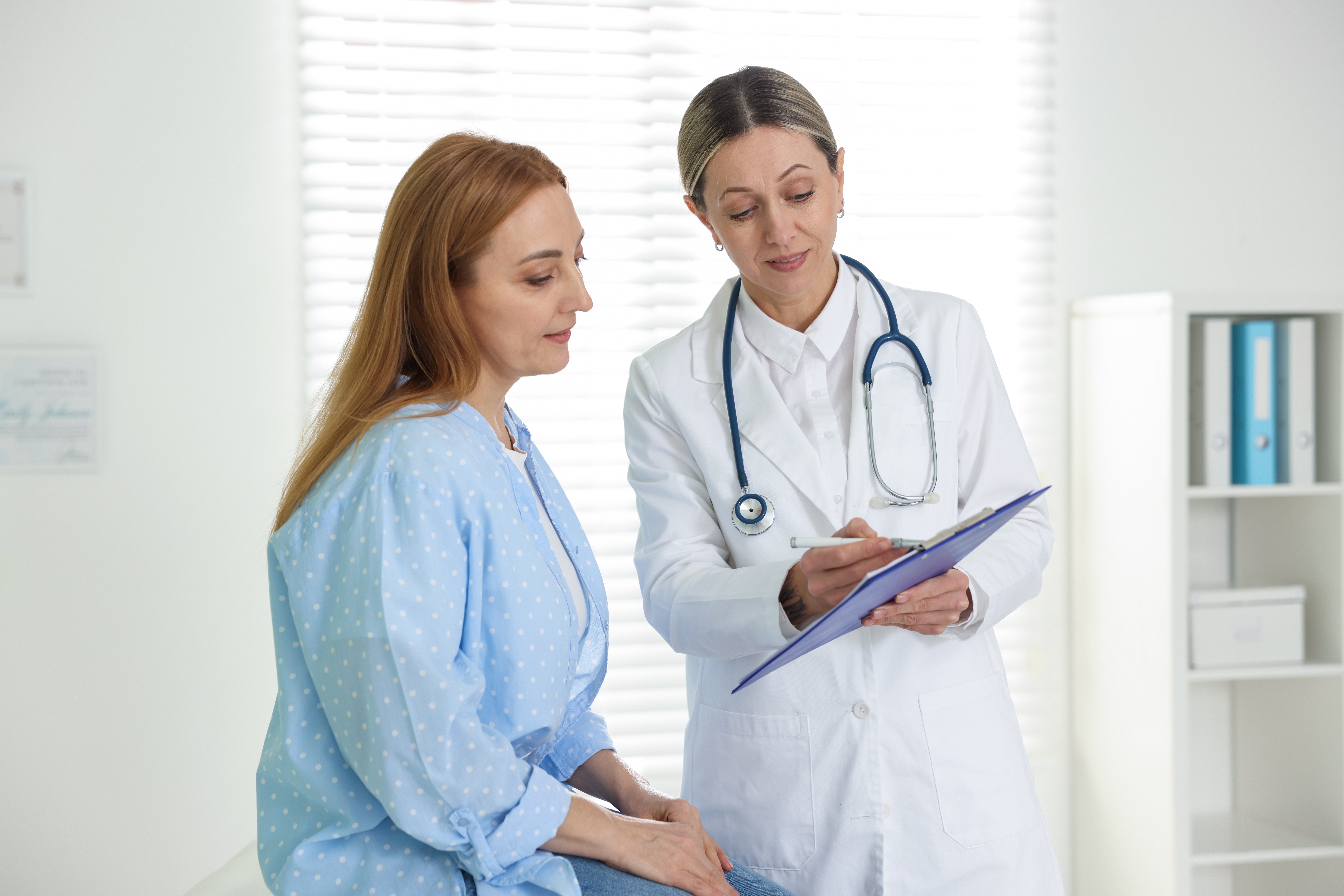 smiling,cardiologist,showing,clipboard,to,patient,in,clinic