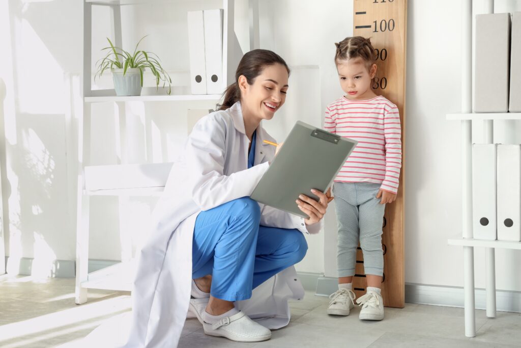 female,pediatrician,with,cute,little,girl,measuring,height,near,stadiometer