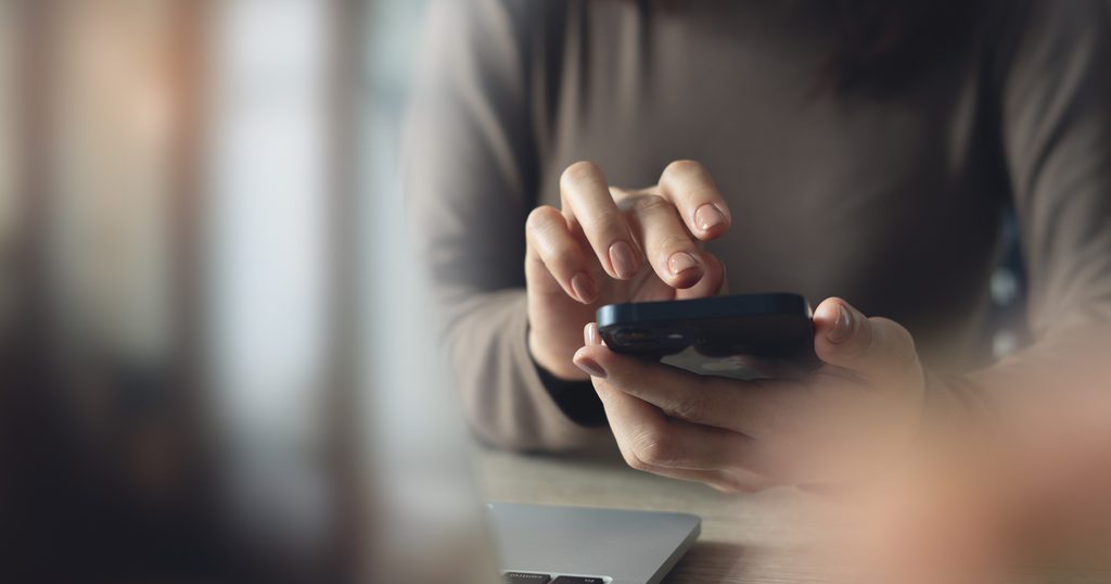 close,up,,business,woman,using,mobile,phone,with,laptop,computer