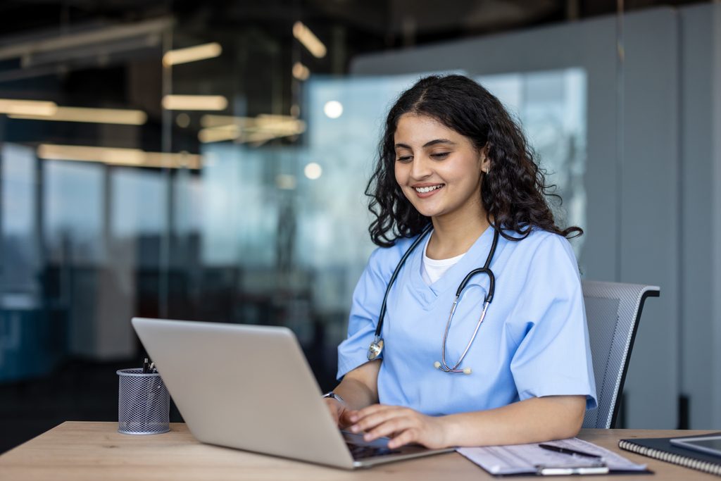 young,smiling,female,medical,professional,in,scrubs,and,stethoscope,working